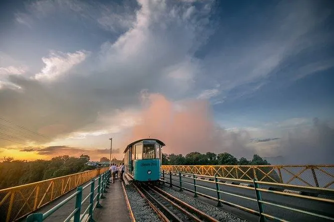 The Bamba Tram crossing the Victoria Falls Bridge at sunset with the Falls' spray rising behind
